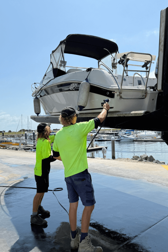 Two Marina workers in hi-vis uniform hosing down a boat.